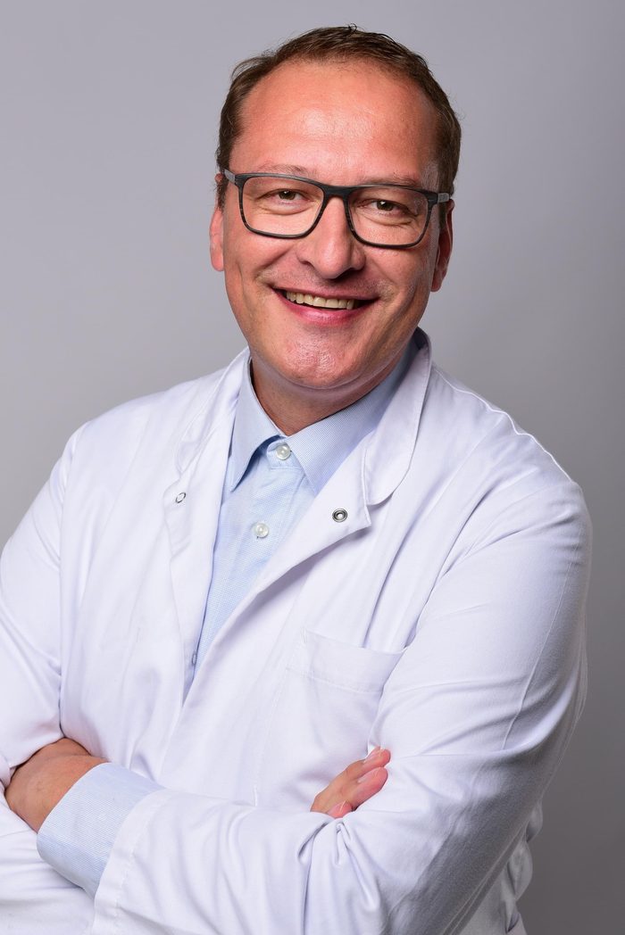 Dr. med. Johannes Link in a white coat, arms crossed, smiling warmly